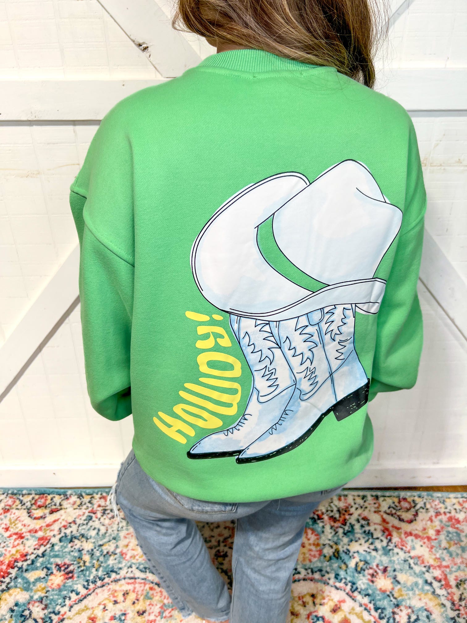 Woman modeling the back of our green sweatshirt showing a cowboy boot and saying Howdy big on the back