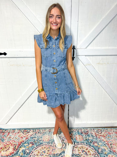 Woman modeling a denim mini dress with cap sleeves and a denim belt. The dress is straight with one ruffle at the bottom