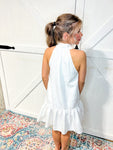 Woman modeling the back of our white sleeveless textured dress that ties in a bow at the neck 