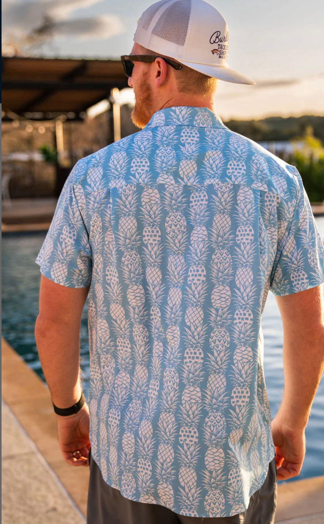 Man modeling the back our light blue, short sleeve button up shirt featuring white pineapples 