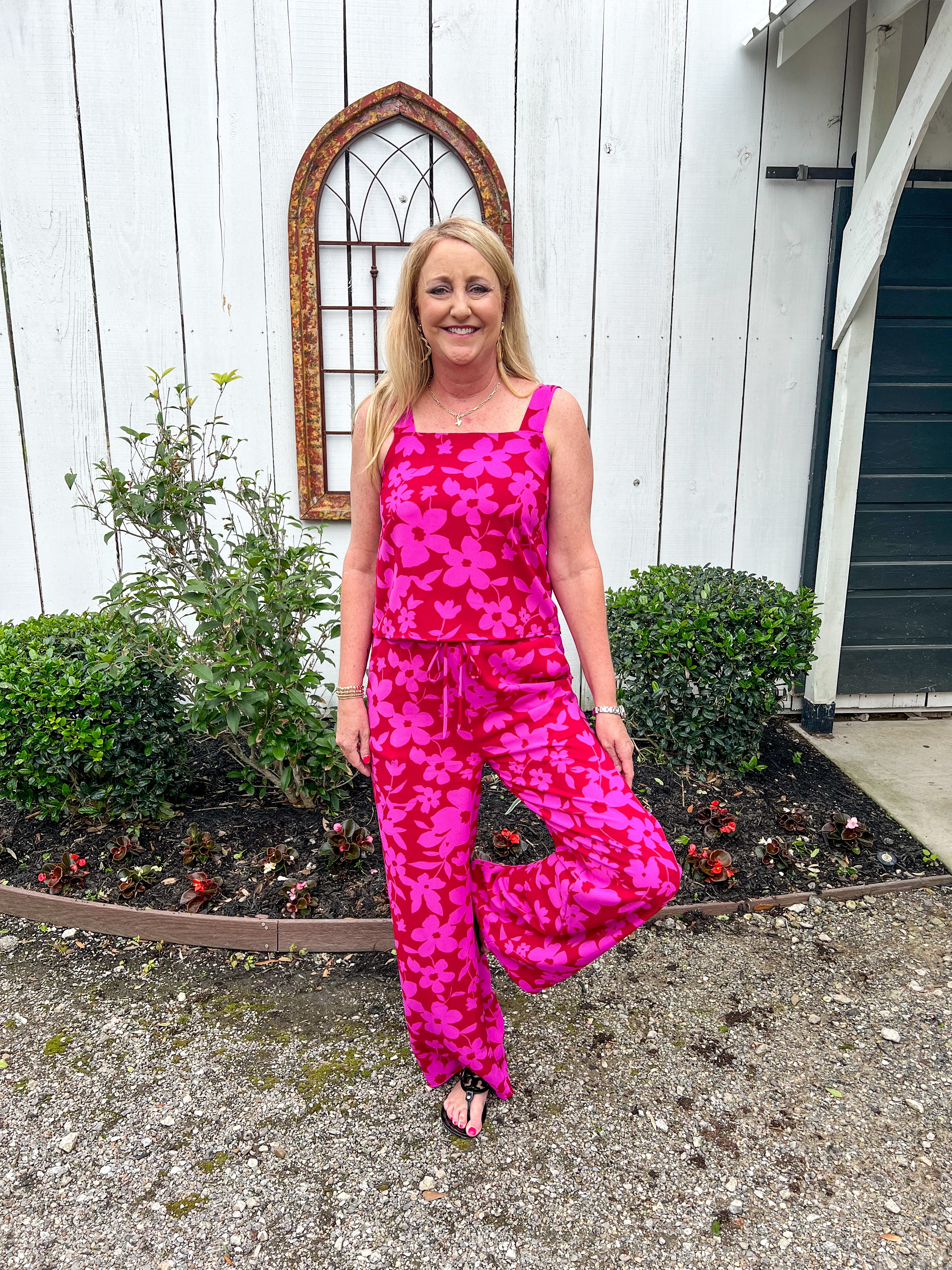 Another photo of a Woman modeling the front of this red with magenta flowers all over matching set which has a tank top and matching elastic pants