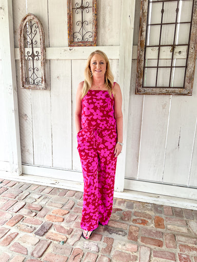 Woman modeling the front of this red with magenta flowers all over matching set which has a tank top and matching elastic pants