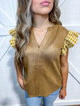 Woman wearing a taupe, v-neck suede-felling blouse with a houndstooth (taupe and cream) ruffle short sleeve