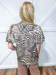 Woman wearing a short sleeve blouse with a relaxed bubble sleeve in a zebra pattern of brown hues
