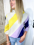 Woman modeling a mock-neck sweater with three quarter sleeves that has thick diagonal stripes in cream, yellow, lavender and navy