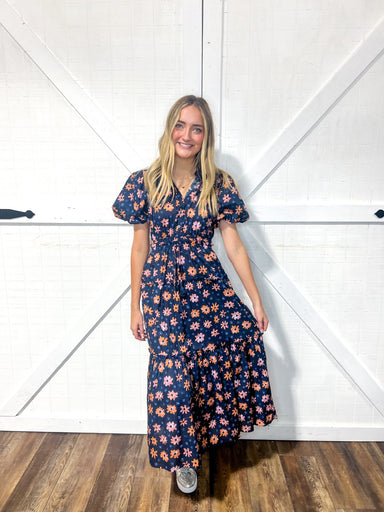 Woman modeling a navy maxi dress w short sleeves with orange and light pink flowers all over.