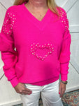Woman modeling a hot pink v-neck sweater with heart shapes covered in pearls