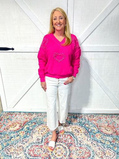 Woman modeling a hot pink v-neck sweater with heart shapes covered in pearls