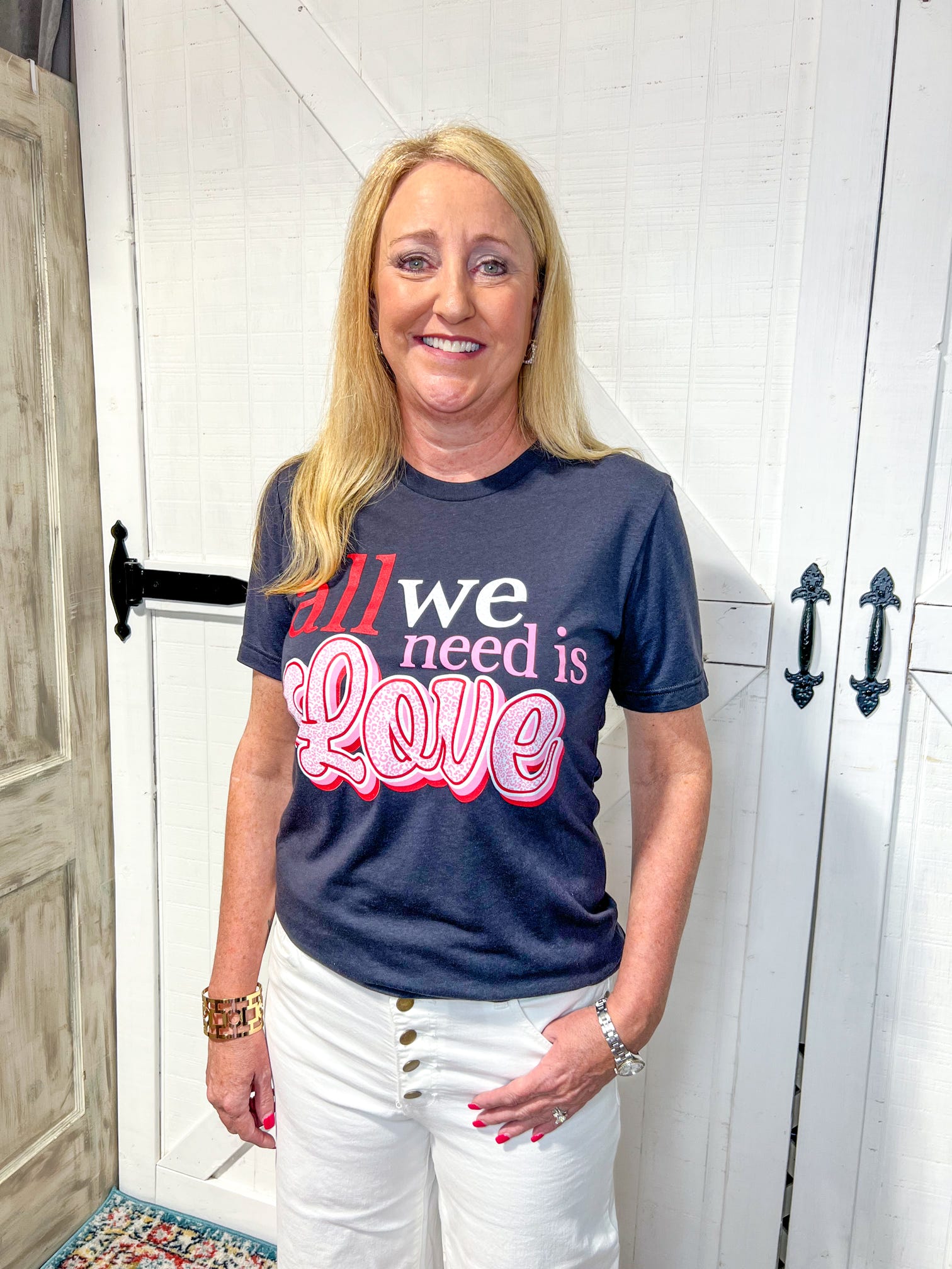 Woman modeling a graphite grey short sleeve tee features a charming red, white, and pink saying of "all we need is Love"
