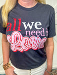 Close up photo of a Woman modeling a graphite grey short sleeve tee features a charming red, white, and pink saying of "all we need is Love"