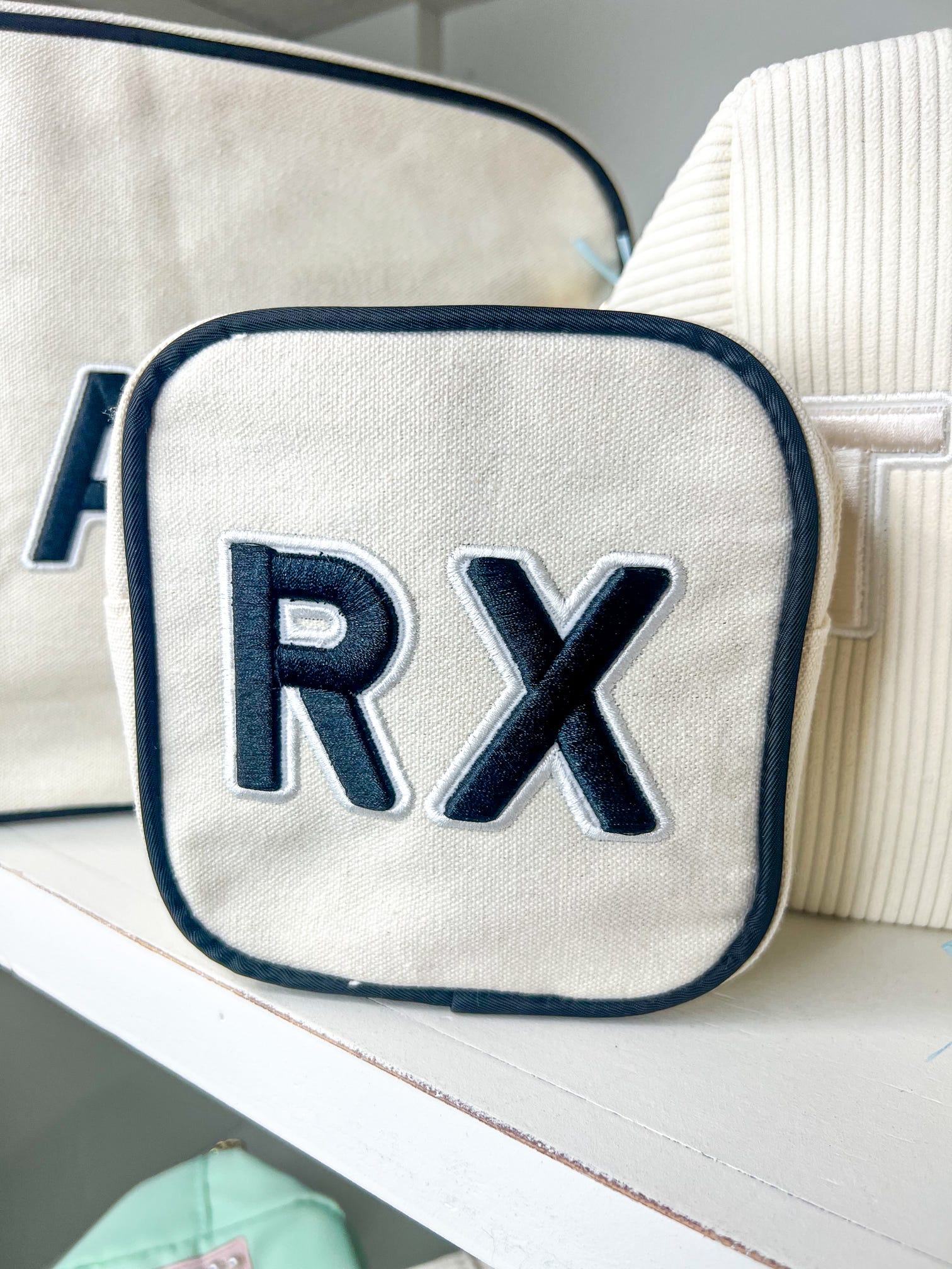 Photo of a compact square cosmetic bag is made of durable canvas and features a bold black 'Rx' on the front.