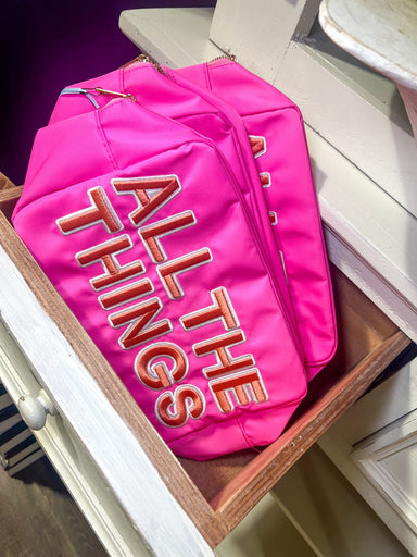 Photo of a hot pink XL canvas makeup bag saying “All the Things” on the front in peach appliqué letters that are sewn on