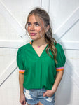 Woman modeling a green v-neck blouse with an orange and pink stripe around the neck and sleeve edge