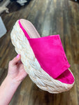 Photo of a magenta side slip-on sandal with a rattan wedge heel. 