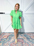 Woman modeling a light green tiered mini dress with a collar, bubble sleeves and gold buttons that button all the way down. 
