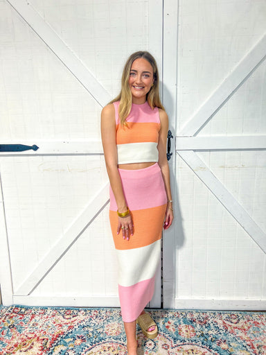 Women modeling a two-piece skirt, set with a sleeveless top and matching long skirt The set has thick vertical stripes in light pink, light orange, and white.
