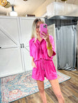 Model taking photo of herself in mirror wearing a two piece shorts set with a short sleeve, button down top and elastic shorts with a tie and big pockets