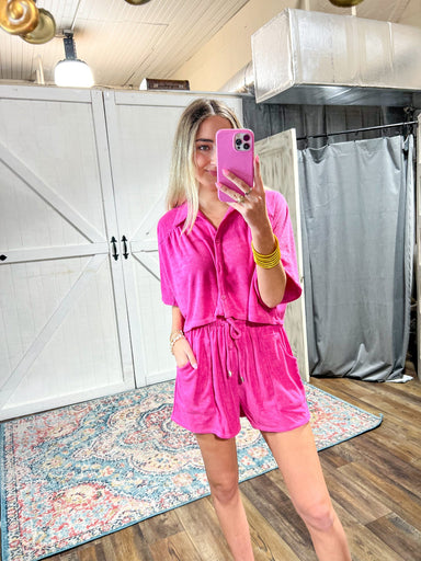 Model taking photo of herself in mirror wearing a two piece shorts set with a short sleeve, button down top and elastic shorts with a tie and big pockets
