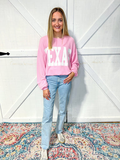 woman modeling our light pink Texas sweatshirt with large white bold letters saying TEXAS across the front