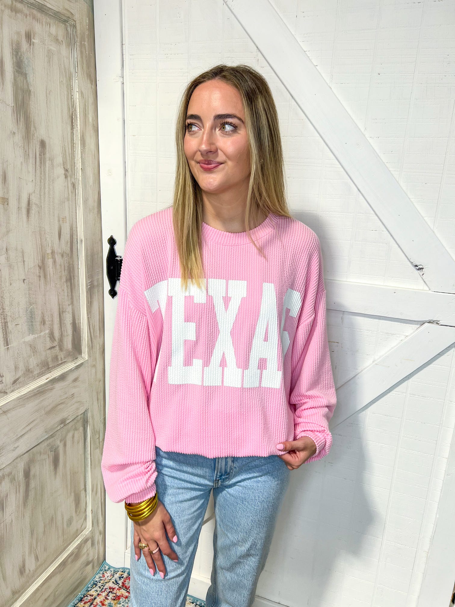 Another view of a woman modeling our light pink Texas sweatshirt with large white bold letters saying TEXAS across the front
