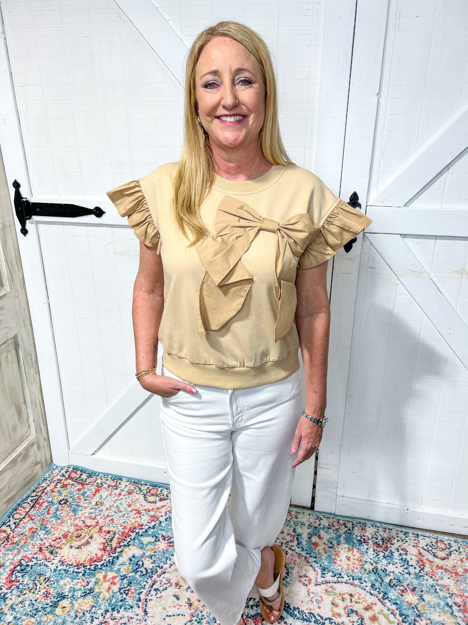 Another photo of a woman modeling our taupe short sleeve top with a ruffle sleeve and a huge bow on the front