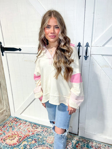Woman modeling a off white v-neck sweatshirt with light pink stripes around the neck and bottom of the sleeves