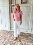 Woman modeling a pink short sleeve top with ruffle sleeves and small pink dots all over (of same color). Top has a band at bottom like a sweatshirt does.