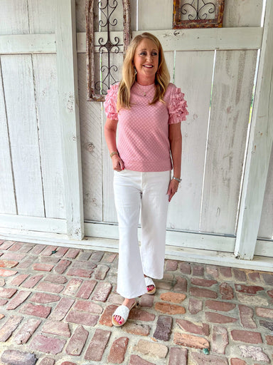 Woman modeling a pink short sleeve top with ruffle sleeves and small pink dots all over (of same color). Top has a band at bottom like a sweatshirt does.