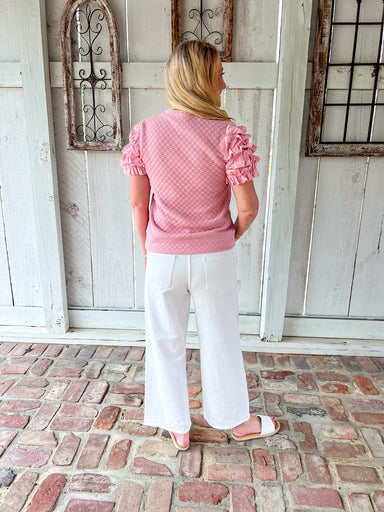Woman modeling the back of a pink short sleeve top with ruffle sleeves and small pink dots all over (of same color). Top has a band at bottom like a sweatshirt does.