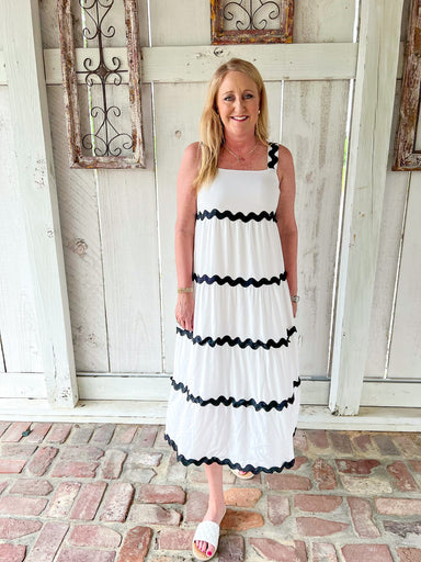 Woman modeling a white sleeveless midi dress with wavy black occasional stripes made of ric rac material
