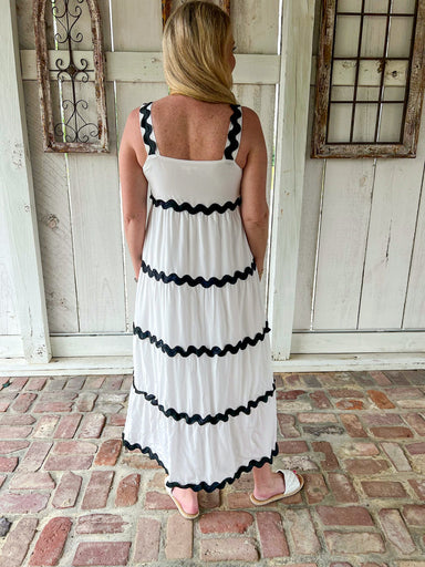 Woman modeling the back of this white sleeveless midi dress with wavy black occasional stripes made of ric rac material