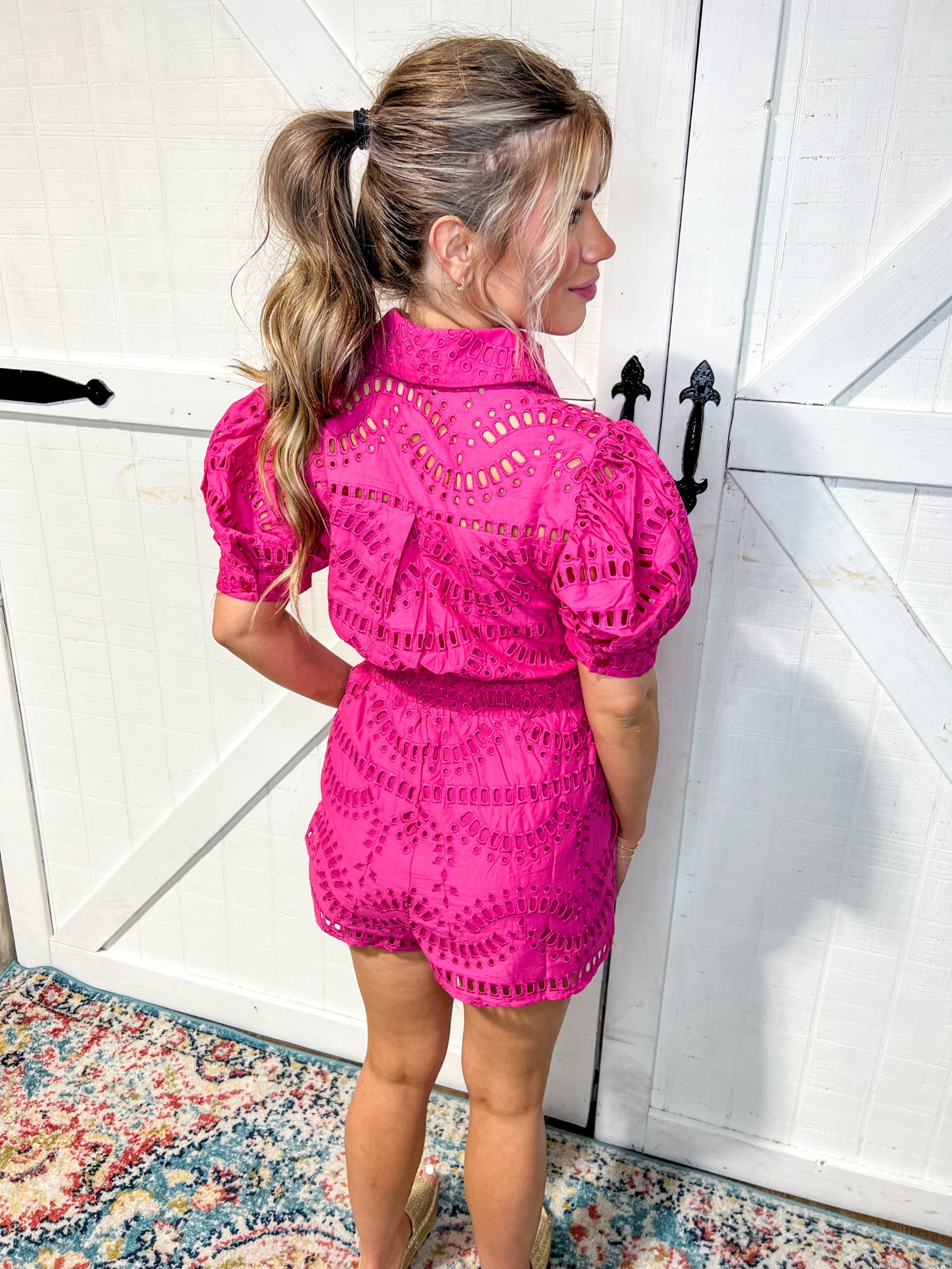 Woman modeling the back of our hot pink/ magenta short sleeve romper with a collar, buttons, cinch waist and attached shorts