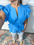 An up close photo of our azure blue short sleeve ruffle sleeve blouse. It has a V-neck and ties at the waist.