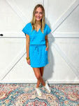 Woman modeling our  matching aqua blue top and mini skirt set featuring a quilted pattern, a v-neck, and short sleeves. 