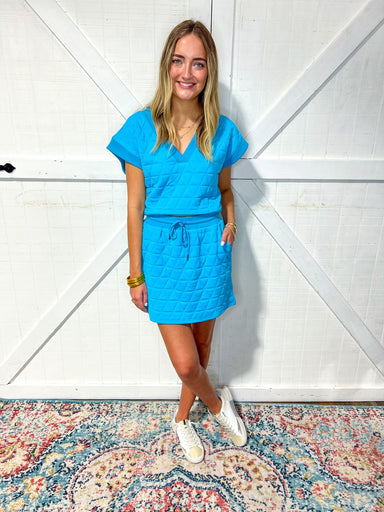 Woman modeling our  matching aqua blue top and mini skirt set featuring a quilted pattern, a v-neck, and short sleeves. 