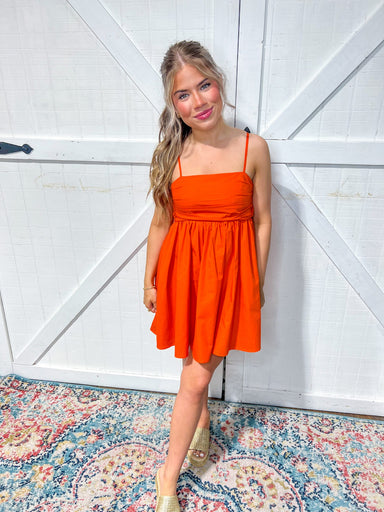 Woman modeling our orange mini dress with spaghetti straps and it ties in a bow in the back