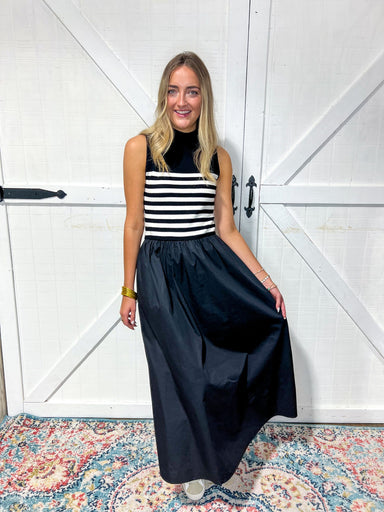 Woman modeling this dress featuring a sleeveless, mock turtleneck black and white stripes in sweater material to the waist with black skirt in polyester material