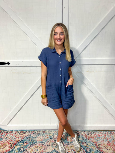 Woman wearing our navy short sleeve romper that has a collar, buttons up and has pockets