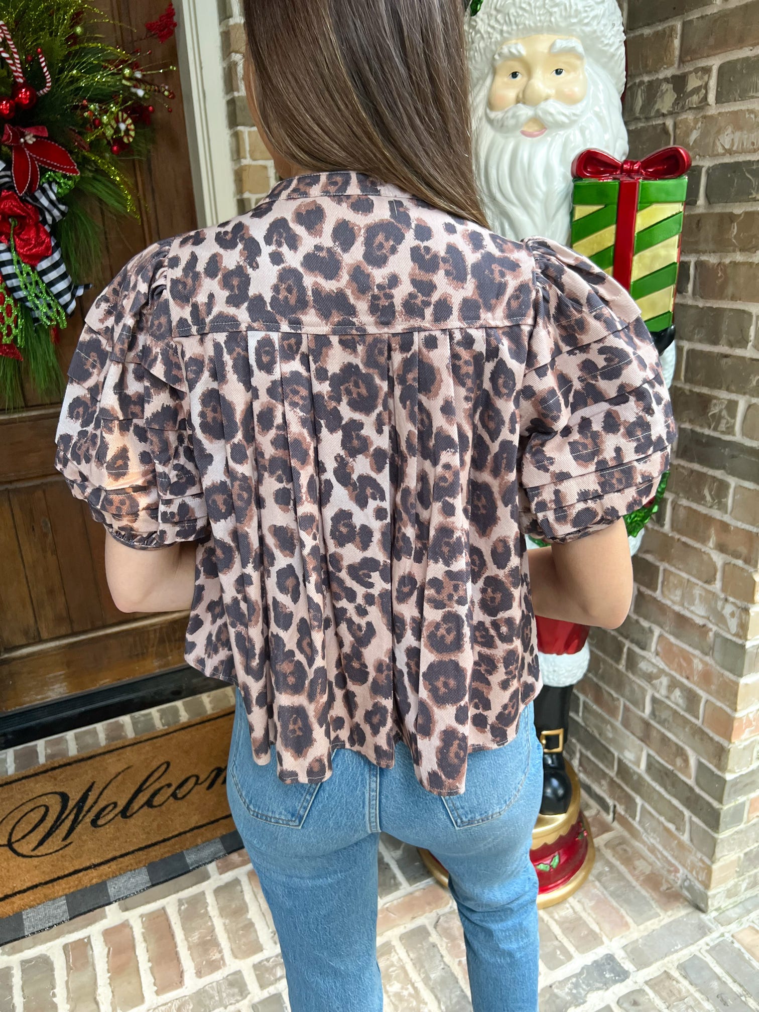 Person wearing a leopard print top with a decorative Santa Claus figure and Christmas decorations in the background.