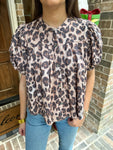 Person wearing a leopard print blouse and blue jeans standing in front of a door.