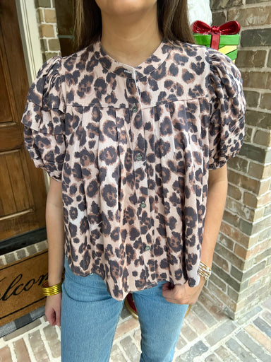 Person wearing a leopard print blouse and blue jeans standing in front of a door.