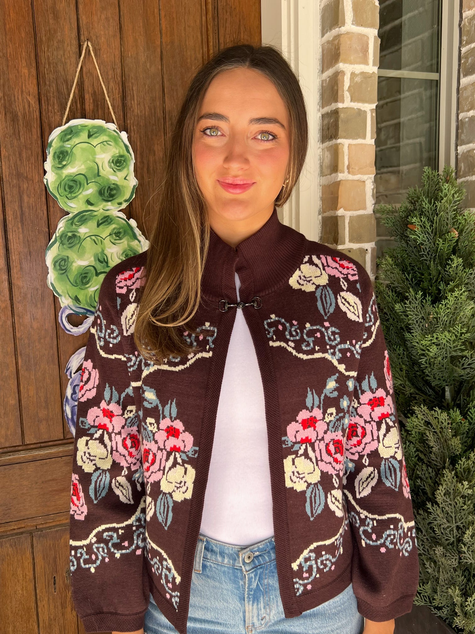 Up close photo of a person wearing a brown floral cardigan with a white shirt and blue jeans, standing outdoors.