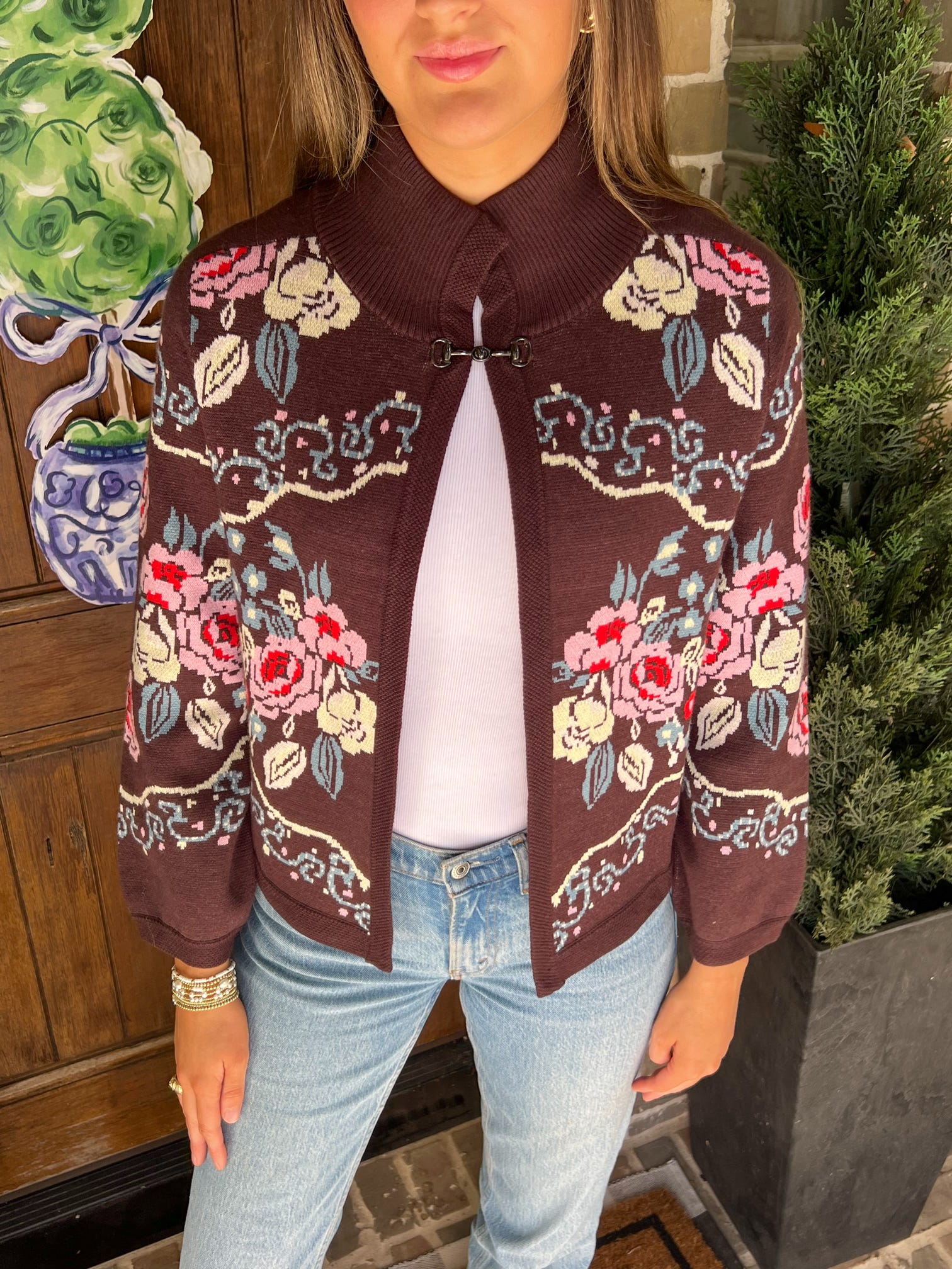 Person wearing a brown floral cardigan with a white shirt and blue jeans, standing outdoors.