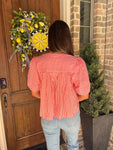 The back of a woman standing in front of a door wearing an orange and white striped blouse