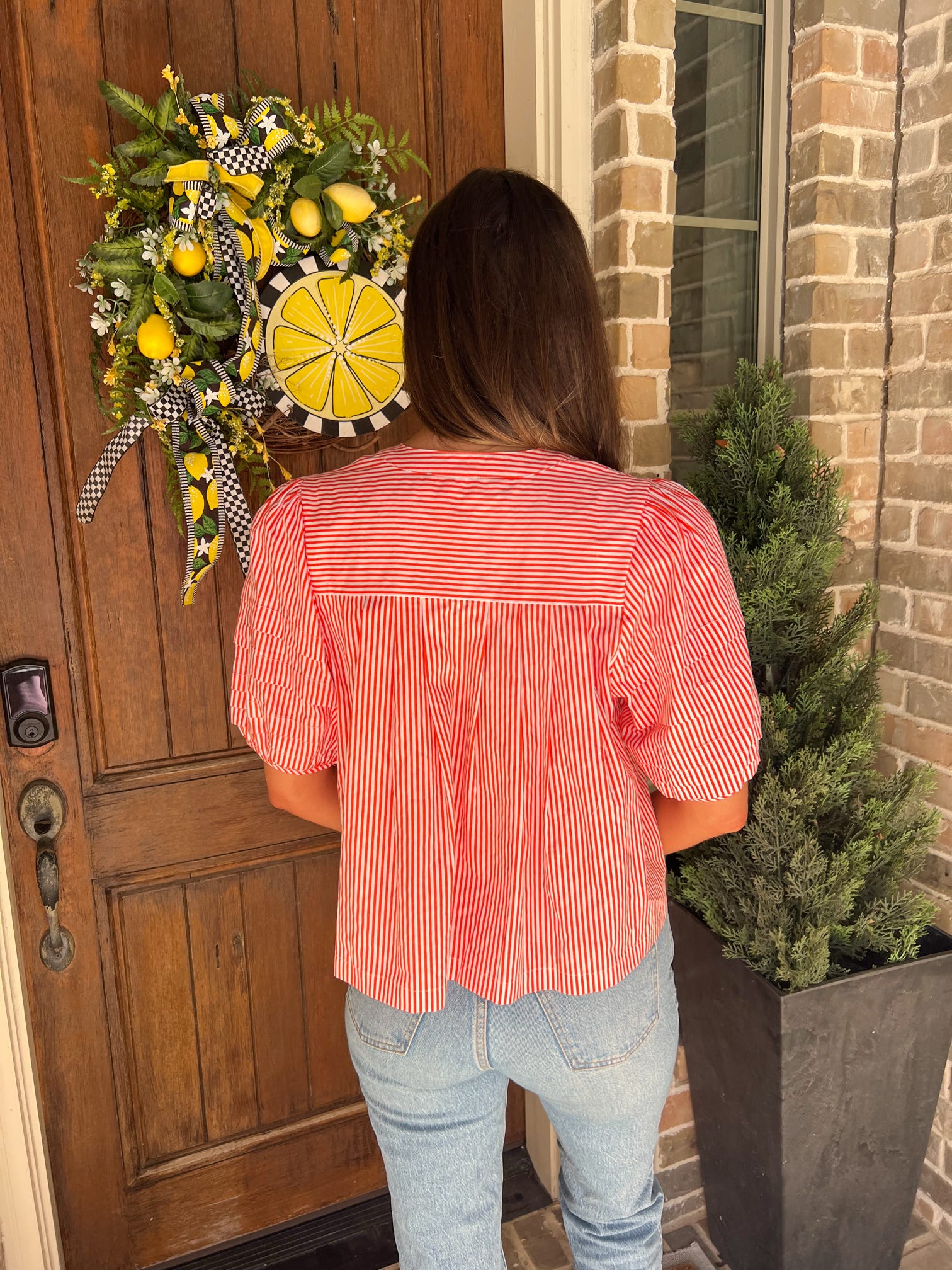 The back of a woman standing in front of a door wearing an orange and white striped blouse