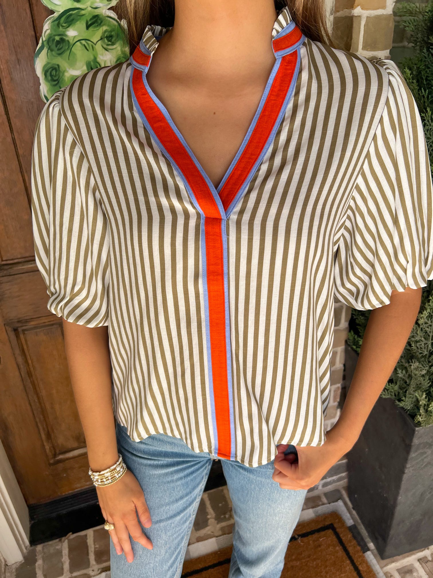 Up close photo of a cream and khaki striped short sleeve blouse with an orange and blue stripe around the collar and down the front 