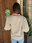 Up close photo of the back of a cream and khaki striped short sleeve blouse with an orange and blue stripe around the collar and down the front 