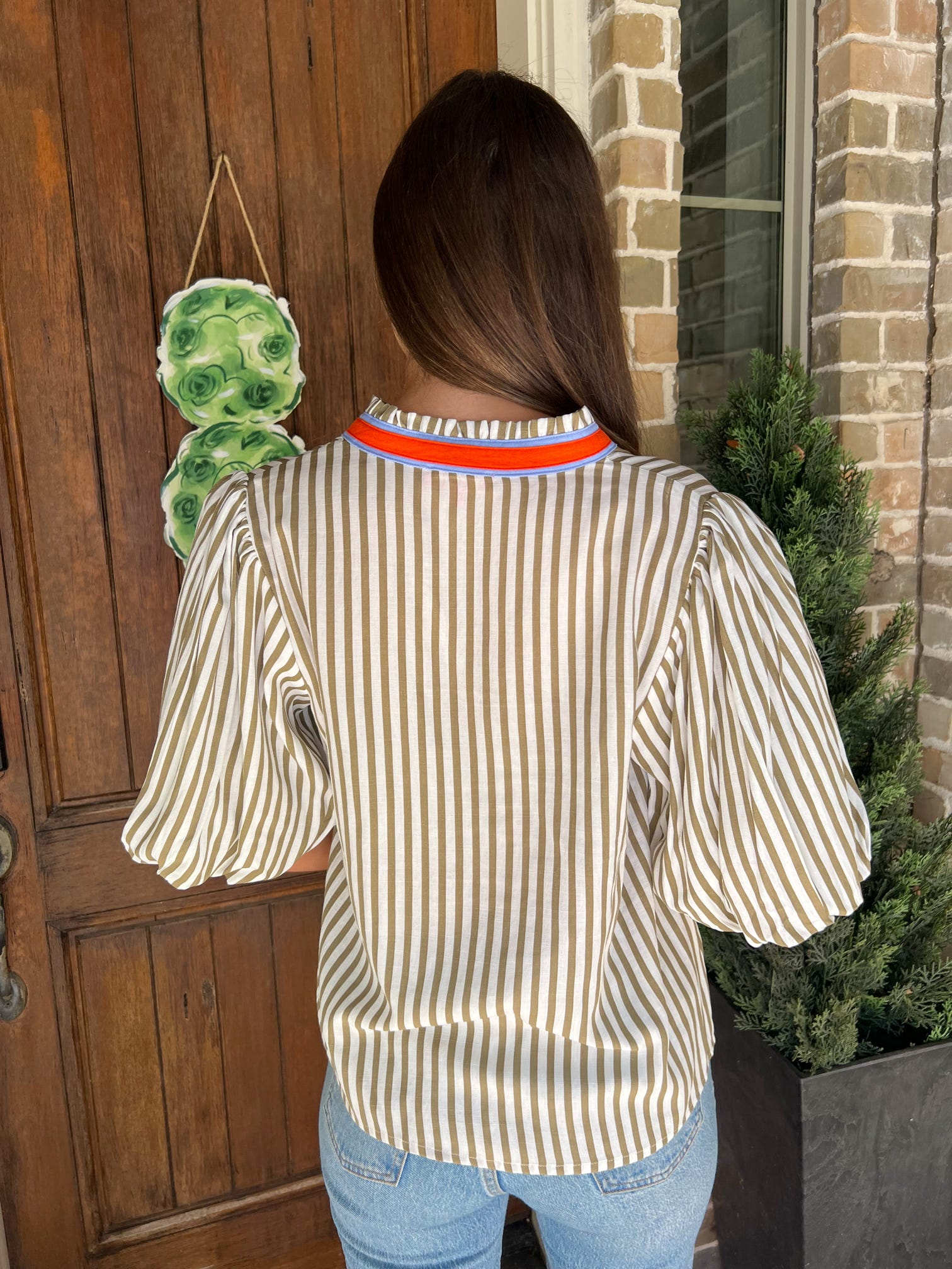 Up close photo of the back of a cream and khaki striped short sleeve blouse with an orange and blue stripe around the collar and down the front 