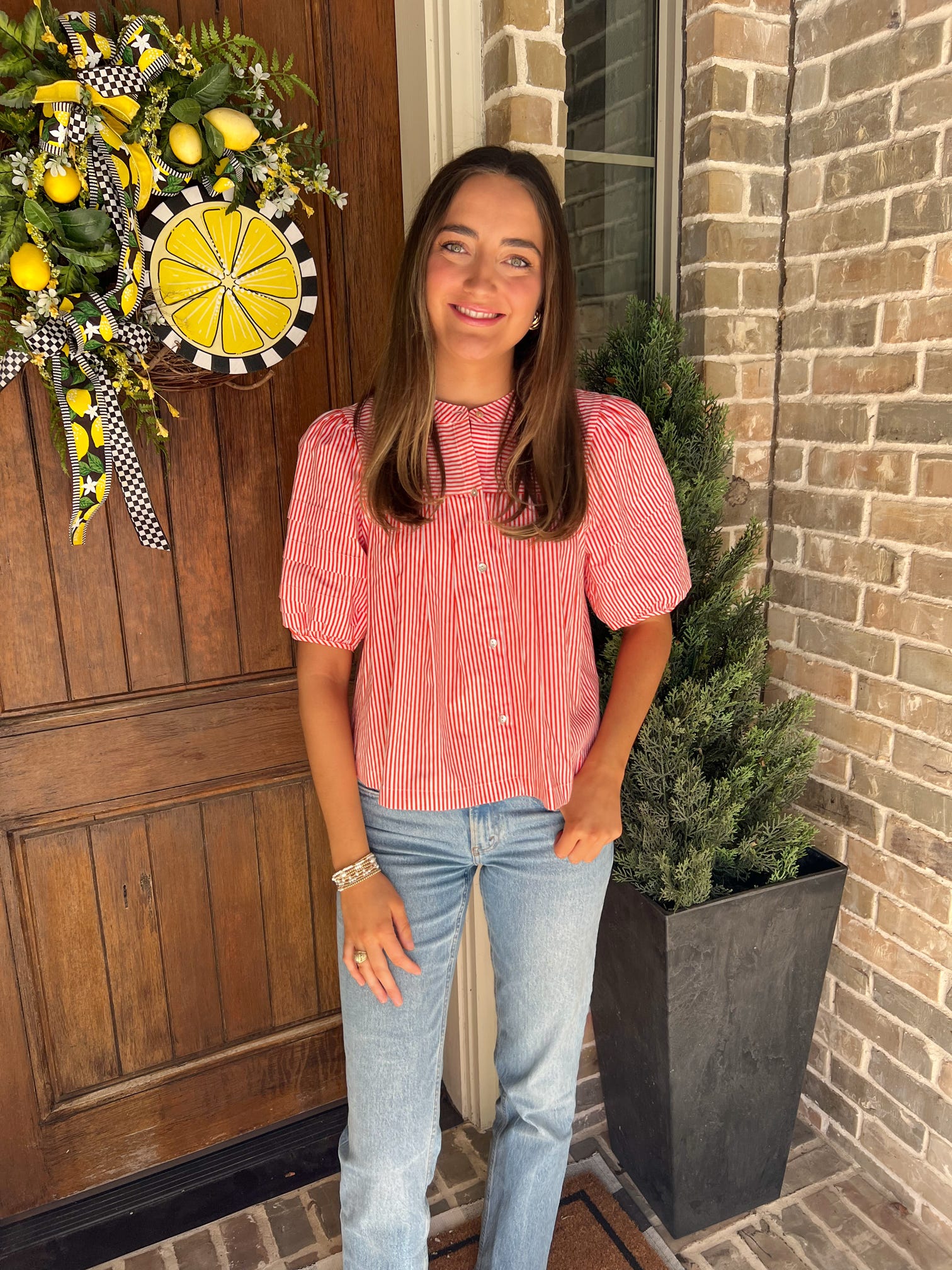 Woman standing in front of a door wearing an orange and white striped blouse