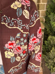 Close-up of the sleeve of a brown cardigan with floral patterns in front of a brick wall.